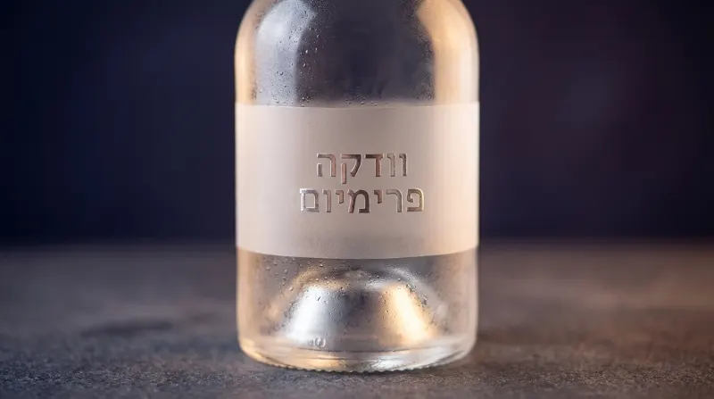 בקבוק זכוכית של וודקה פרימיום עם תווית לבנה וכתב עברי, מכוסה באגלי טל